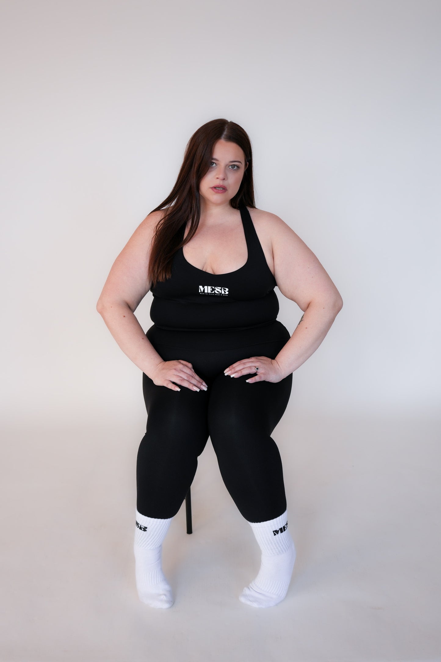 Model sitting on black stool wearing the obsidian obsession MESB tank top set and MESB socks